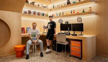 Squeezie pose dans son studio moderne. L'endroit semble professionnel et bien équipé : étagères rétroéclairées, objets de collection et matériel informatique.